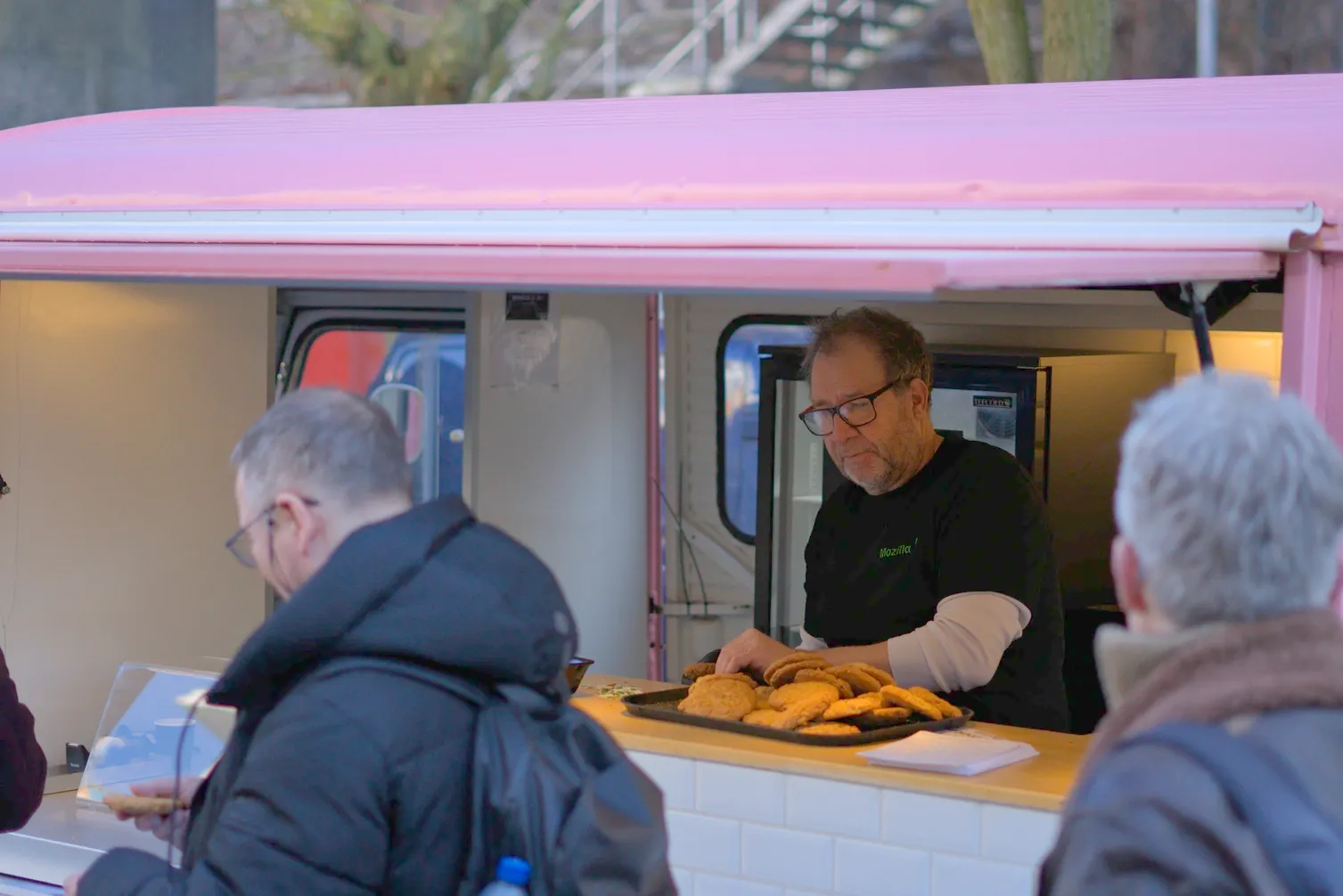 A photo of a person inside a pink food truck giving cookies to visitors.